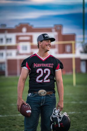Football player in black Panthers jersey posing on field with equipment and stadium in background.