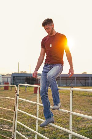 Person in jeans walking along white fence posts at sunset with golden light.