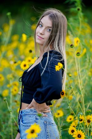 Portrait in field of yellow wildflowers wearing navy top and jeans.