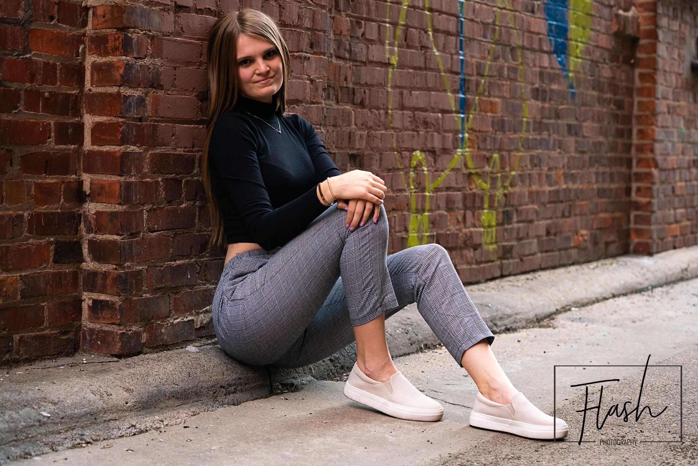 Casual portrait session against a rustic brick wall with colorful graffiti accents.