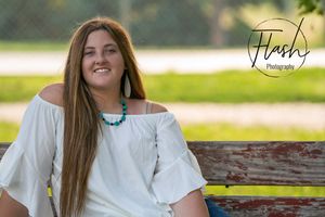 Person in white top sits on wooden bench during outdoor summer photo session.