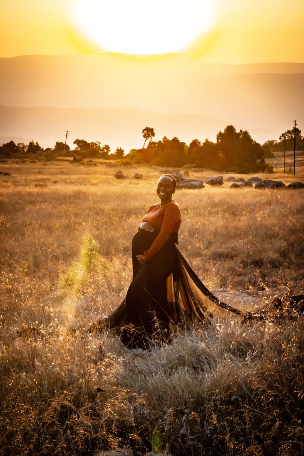 pregnant woman holding belly in field sunset maternity dress glow photography