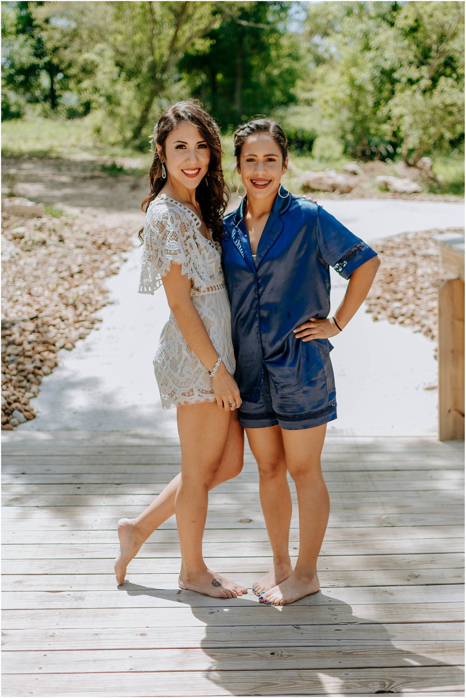 Two people posing on wooden deck surrounded by lush greenery.