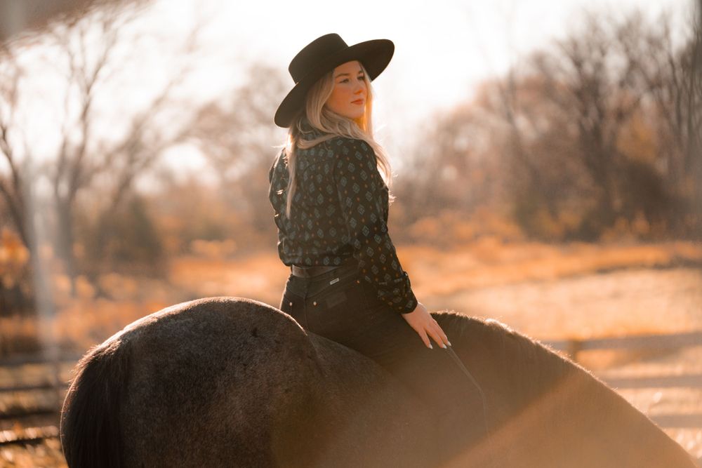 Silhouette of a horse rider in a wide-brimmed hat against an autumn sunset.