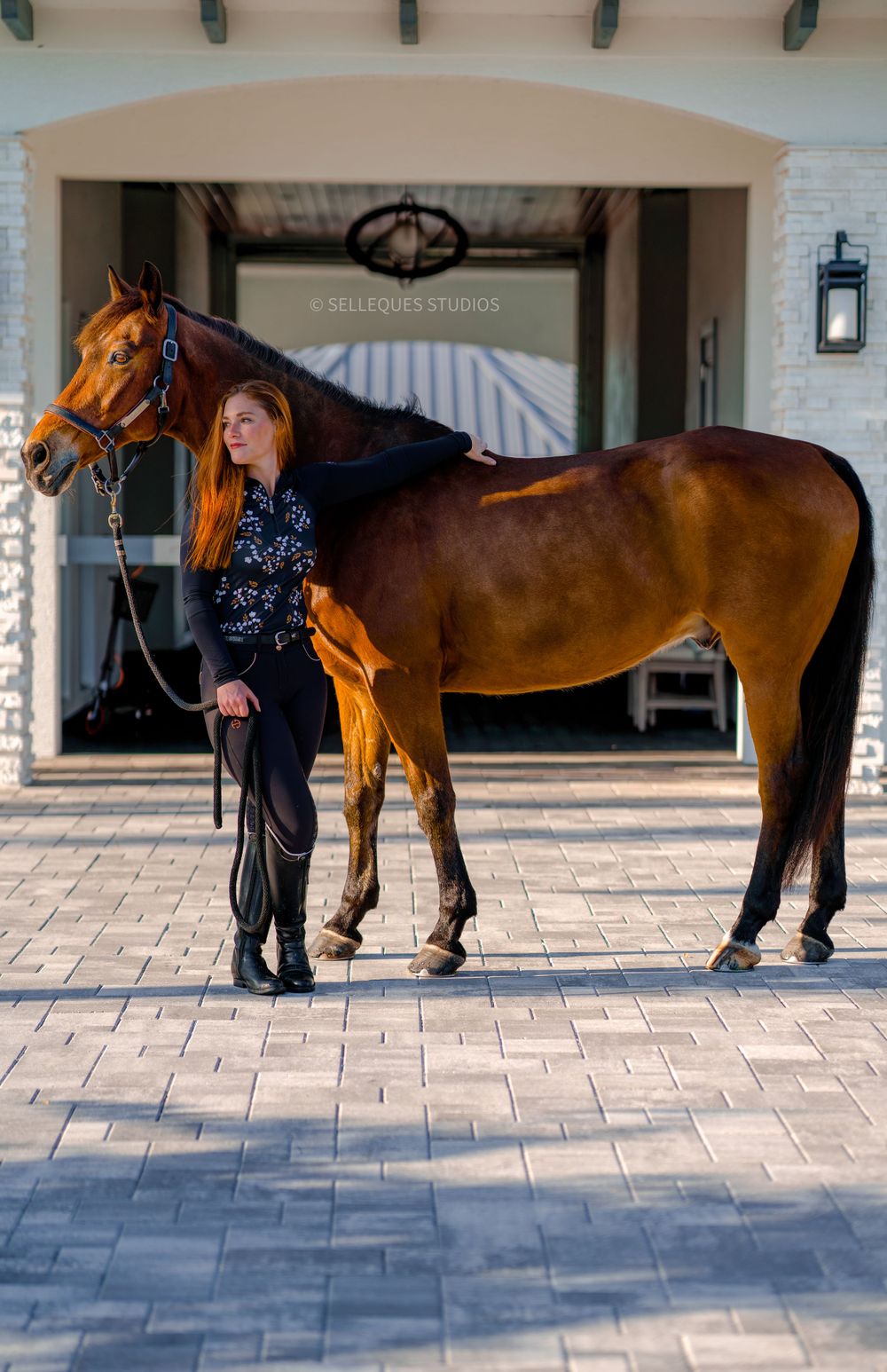 Beautiful bay horse and handler posing in front of elegant white brick building.