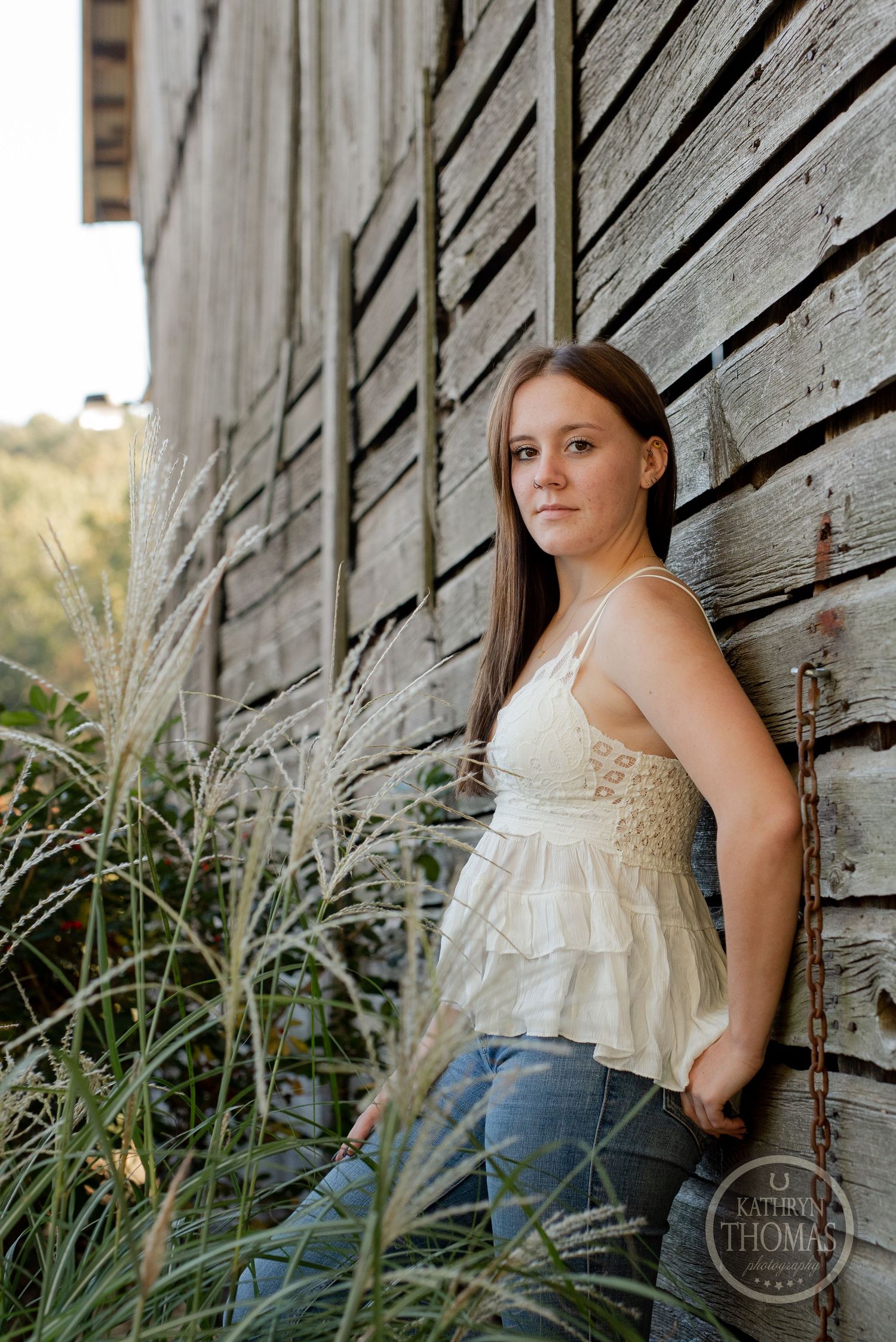 Natural light portrait against textured wooden barn siding with tall grass.