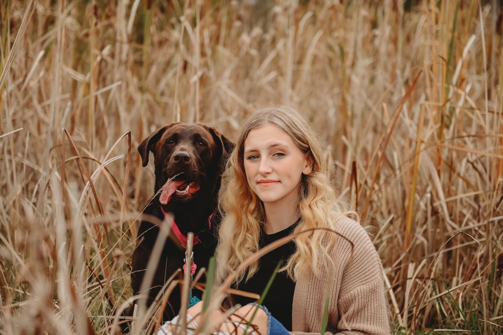 Portrait of person with black Labrador retriever in tall autumn grass.