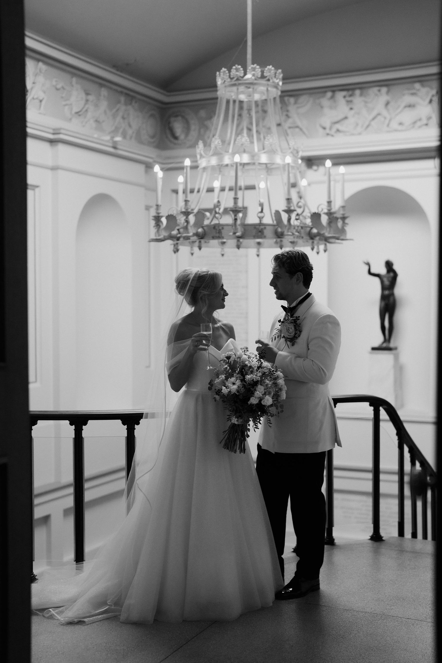 bride and groom stood at top of the stairs with champagne in the ashmolean museum