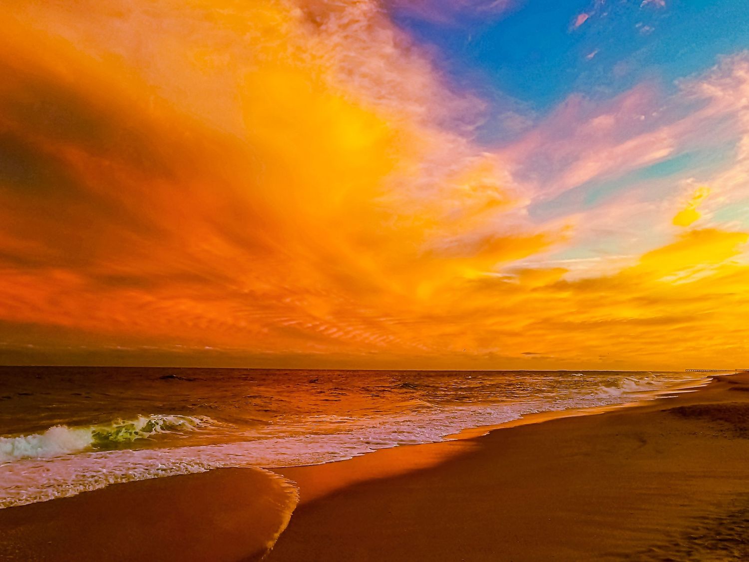 Dramatic orange and purple sunset sky over beach with waves crashing on sandy shore.