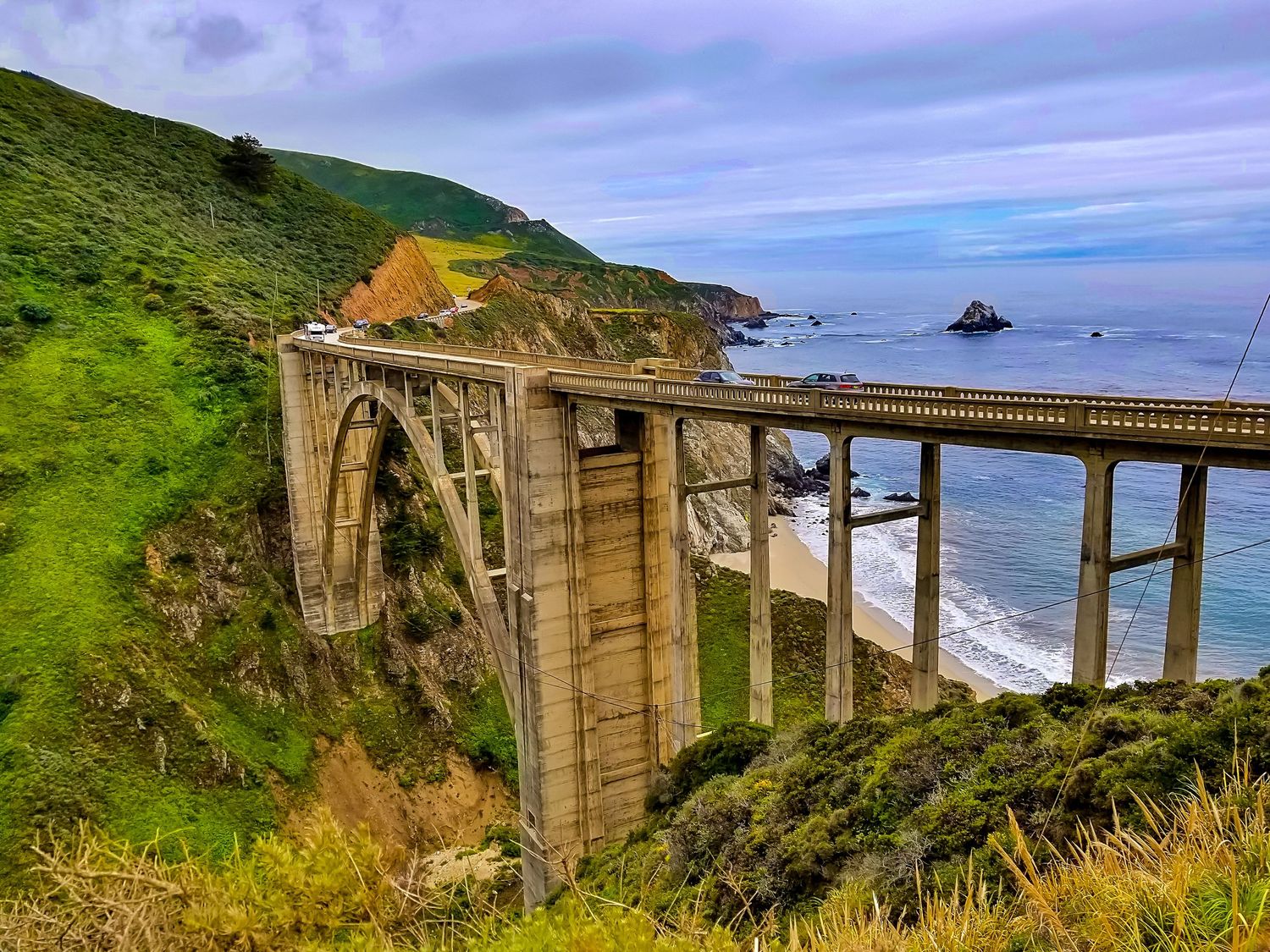 Historic Bixby Creek Bridge spans dramatic California coastline with waves crashing below.