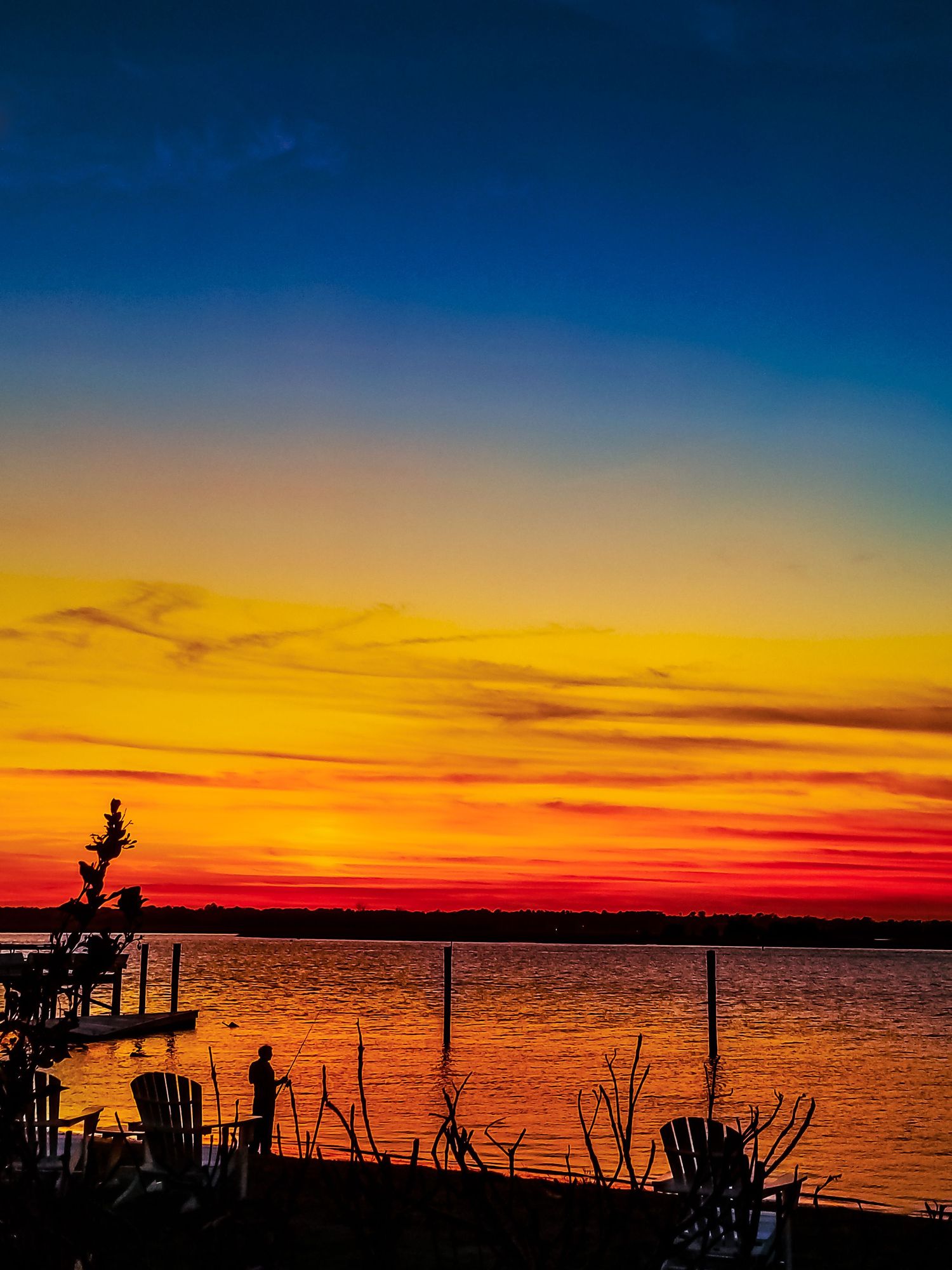 Silhouetted dock structures against brilliant orange and yellow sunset over calm water.