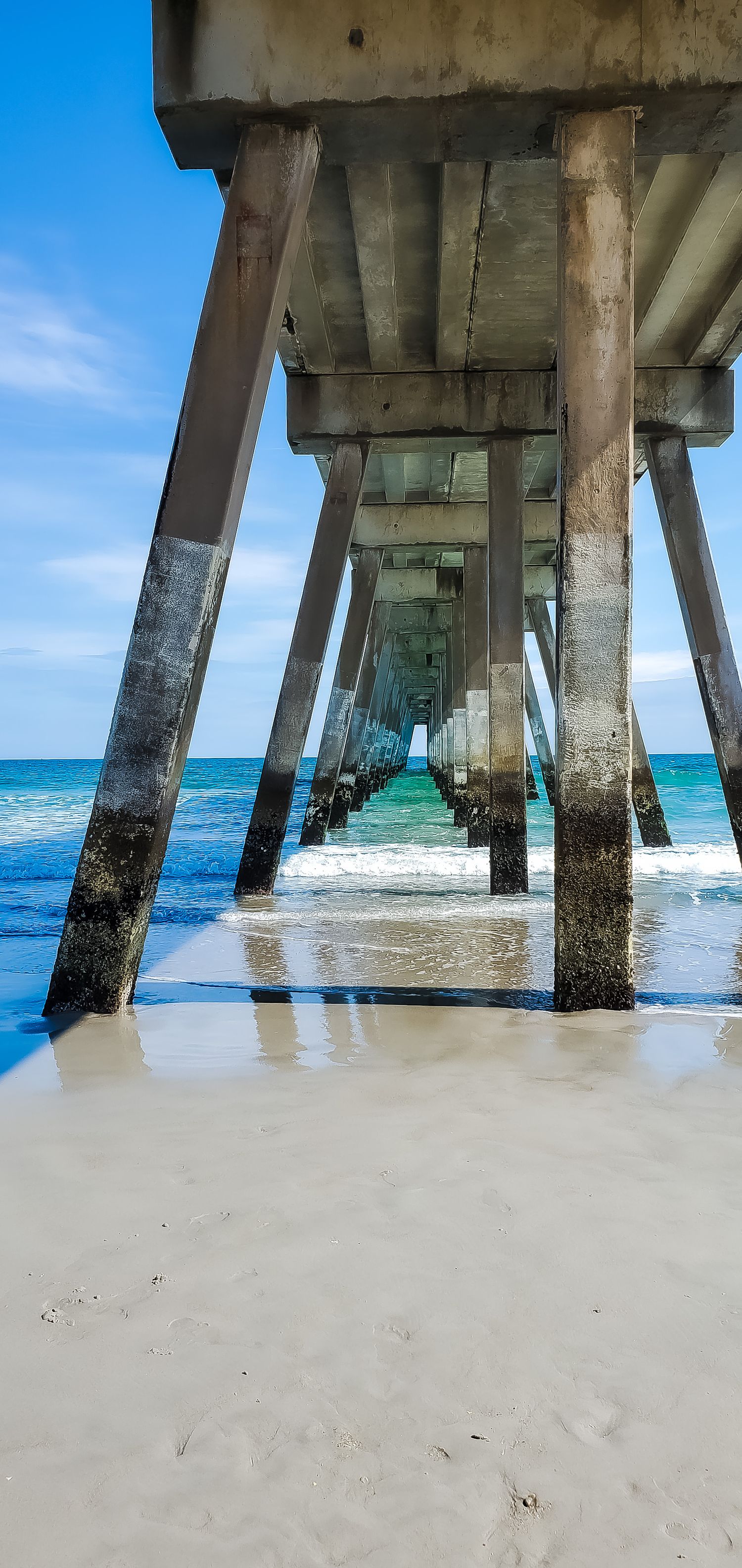 Underneath view of concrete pier supports extending into turquoise ocean waters.
