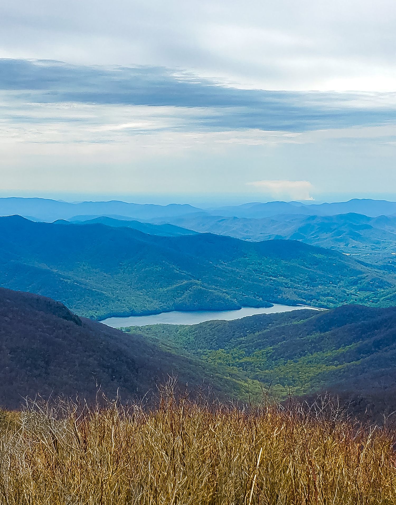 Misty blue mountain ranges stretch into the distance with a lake nestled in the valley below.
