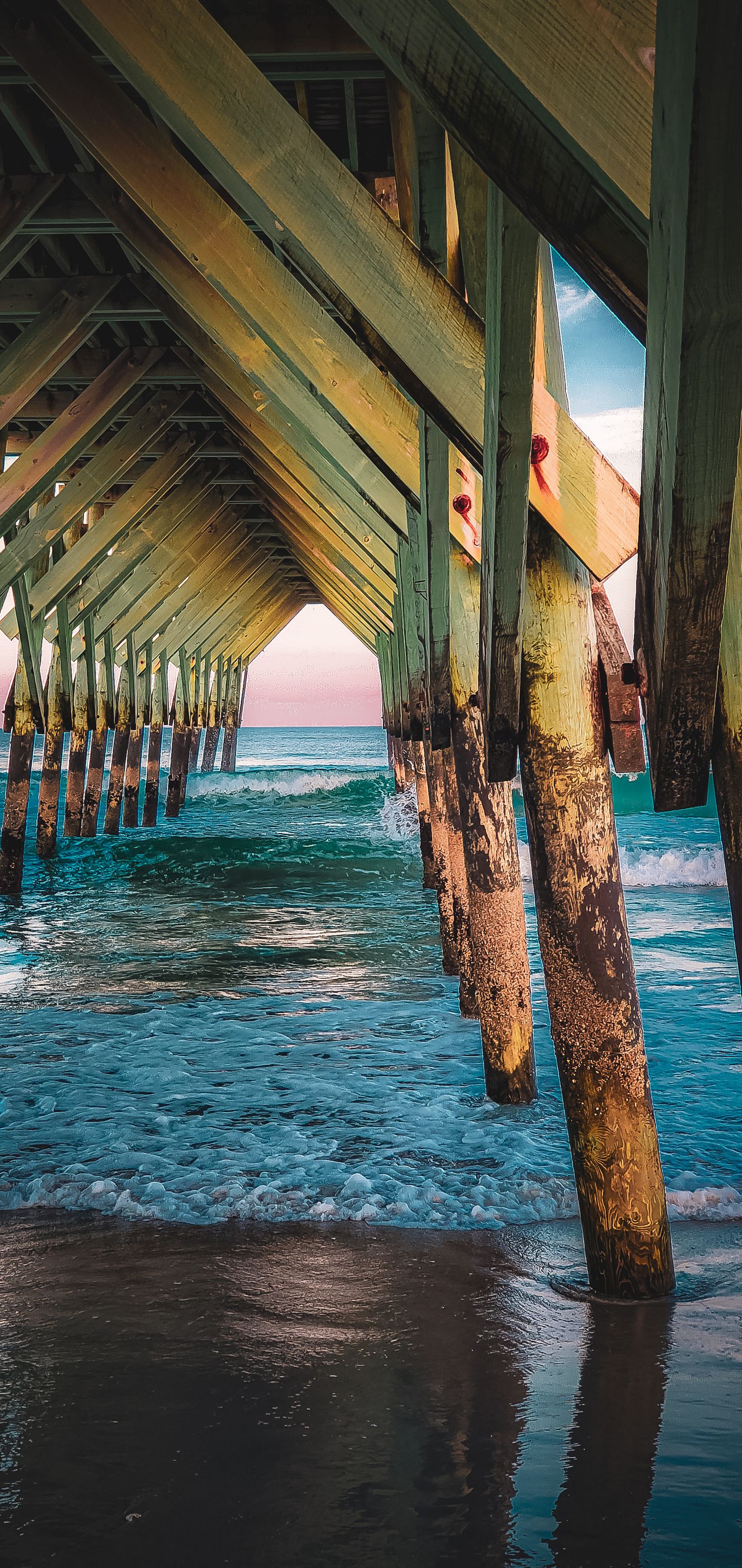 Weathered wooden pier pillars stretch into turquoise ocean water during sunset.