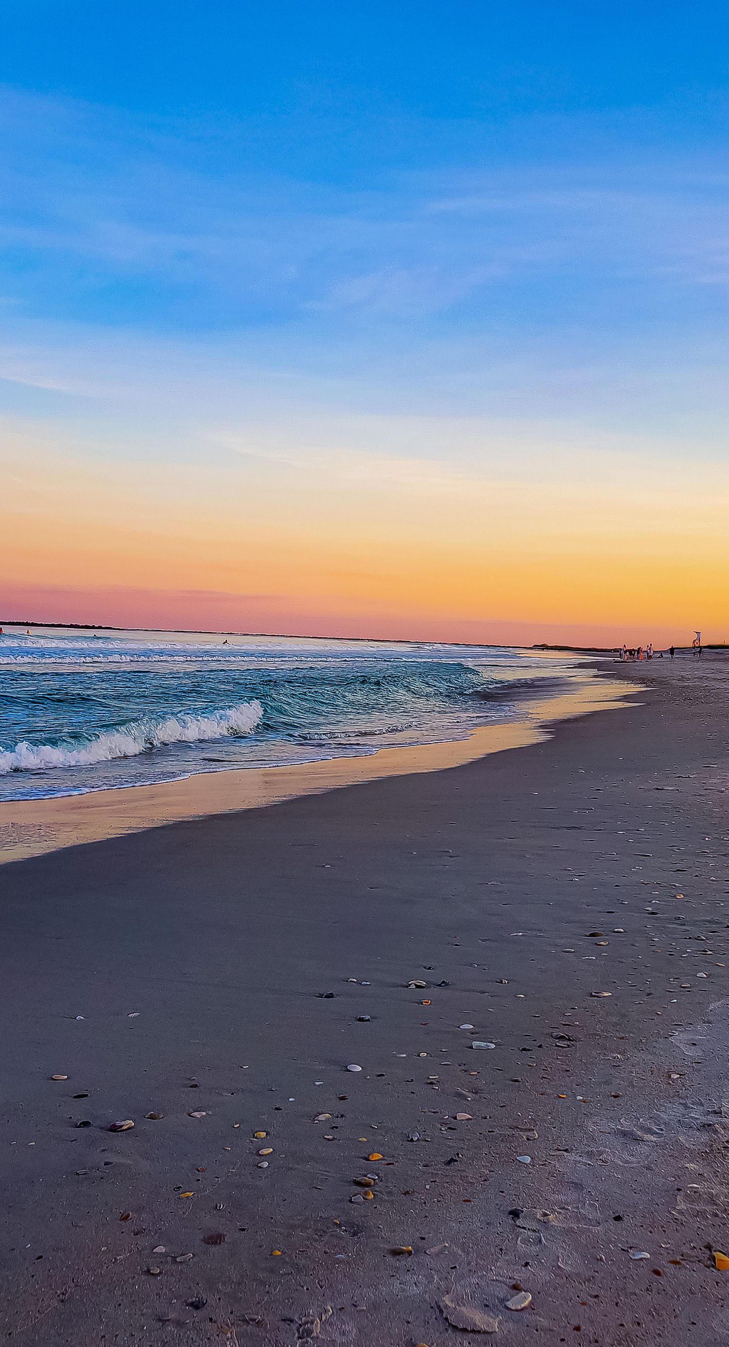 Peaceful beach scene with gentle waves rolling onto shore during a pastel sunset.