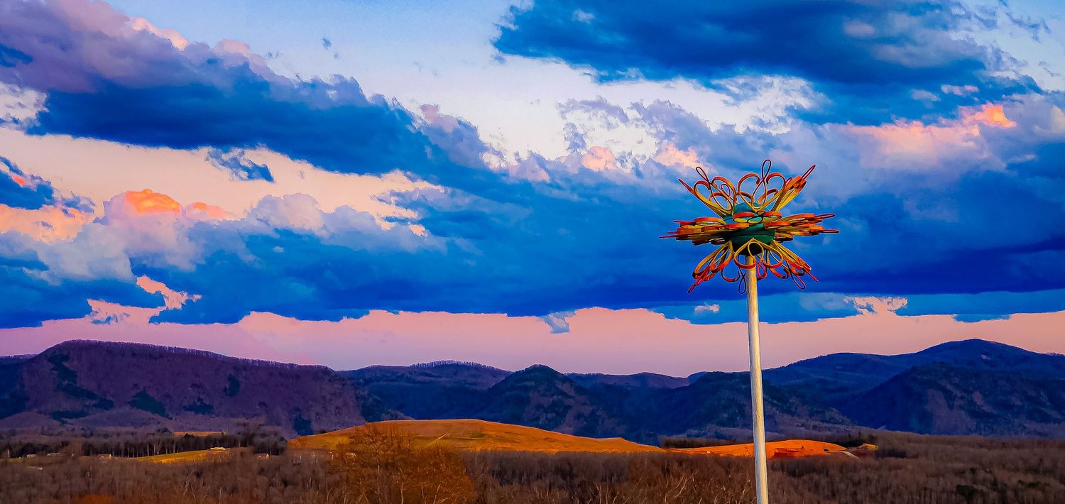 Single palm tree silhouetted against dramatic sunset sky with mountains in background.