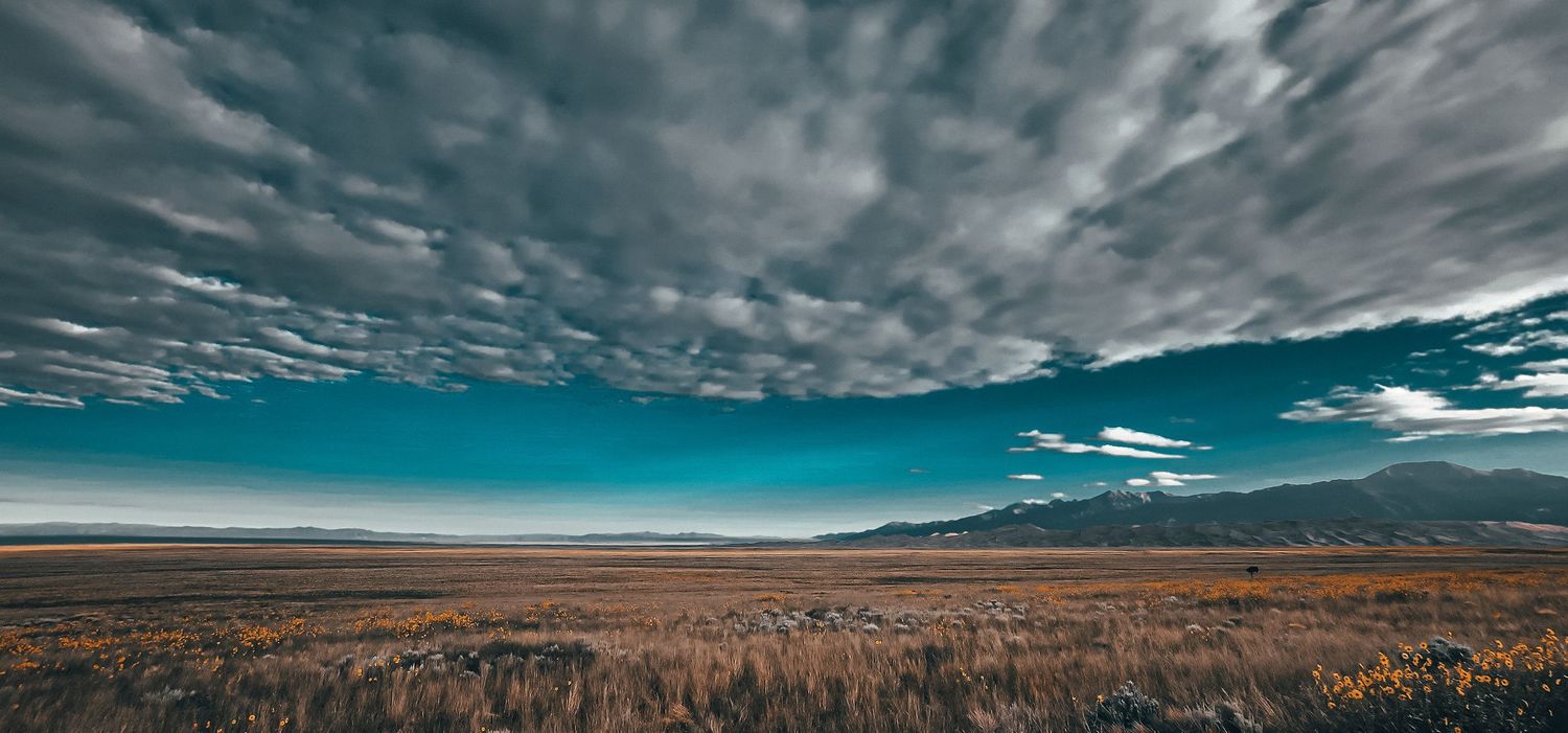 Dramatic wide desert landscape under striking turquoise sky with layered altocumulus clouds.