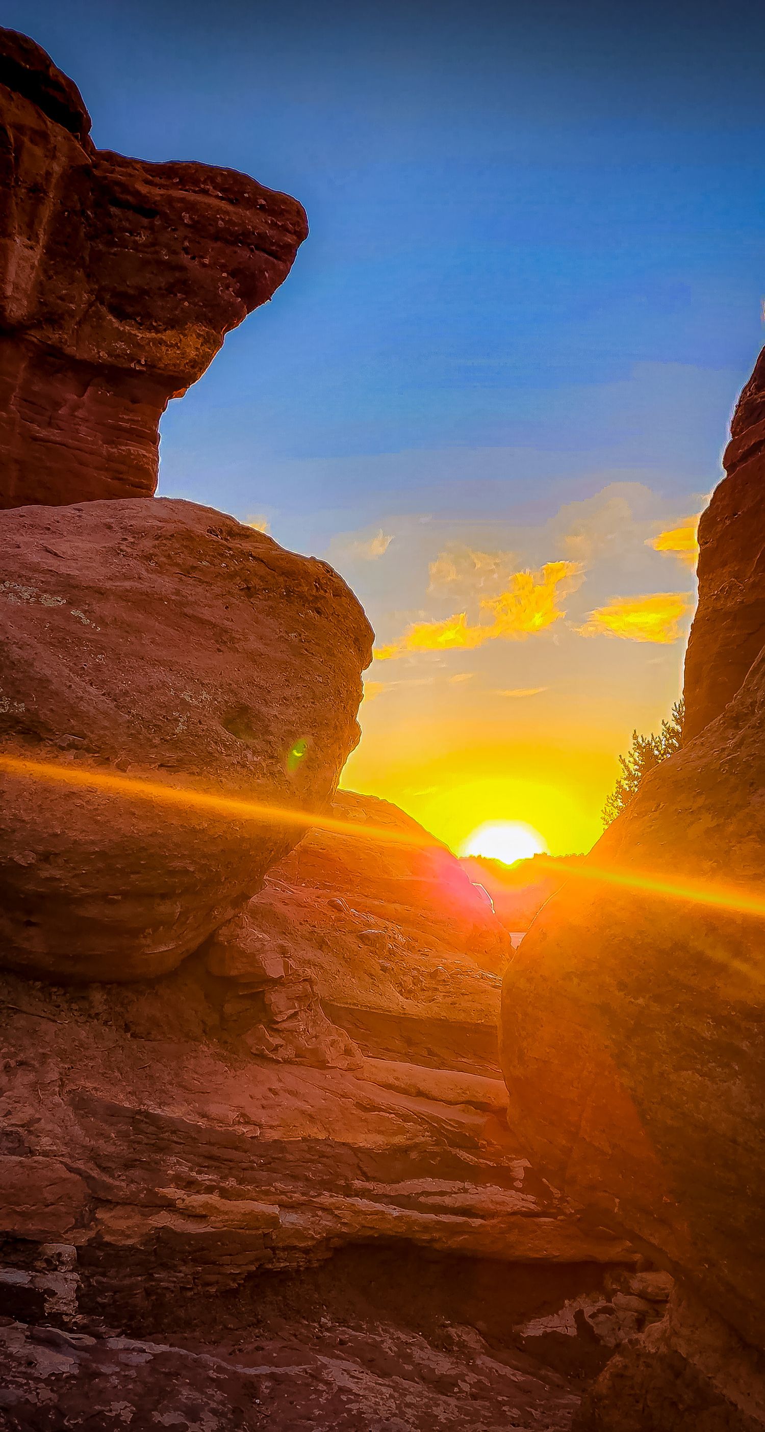 Golden sunset glows between towering red rock formations in desert landscape.