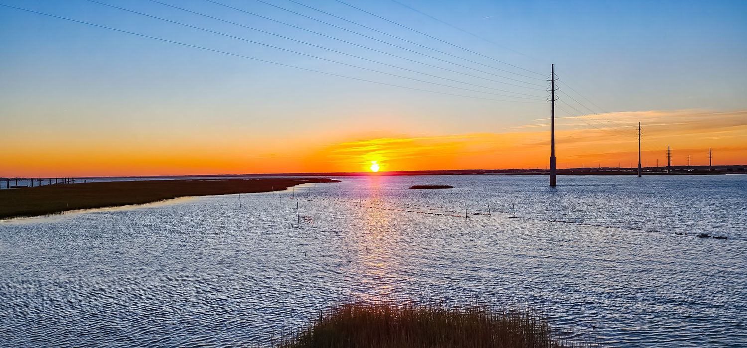 Vibrant sunset over coastal waters with utility poles silhouetted against orange sky.