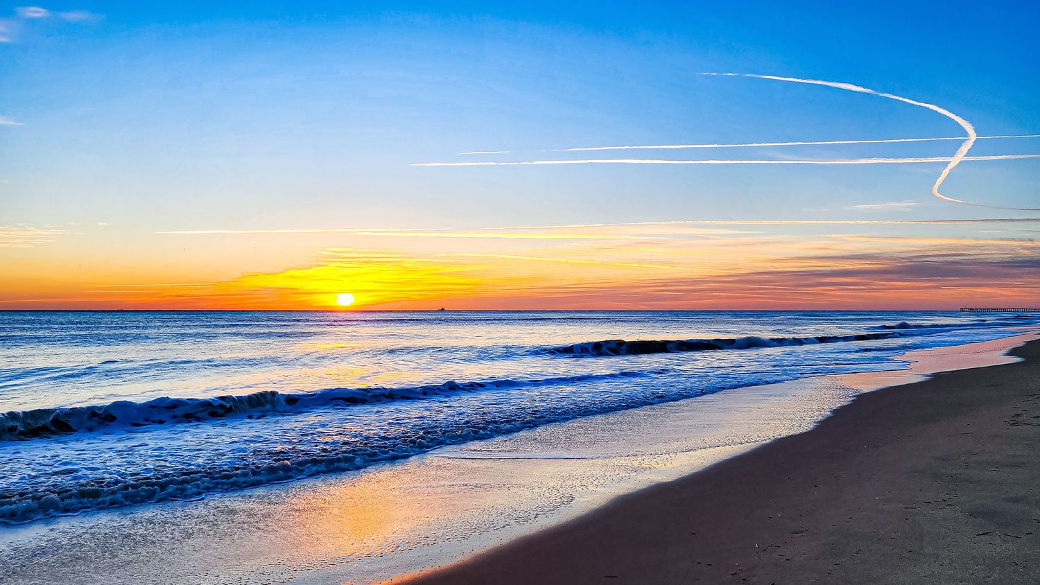 Vibrant orange sunset over ocean horizon with waves breaking on sandy beach shore.