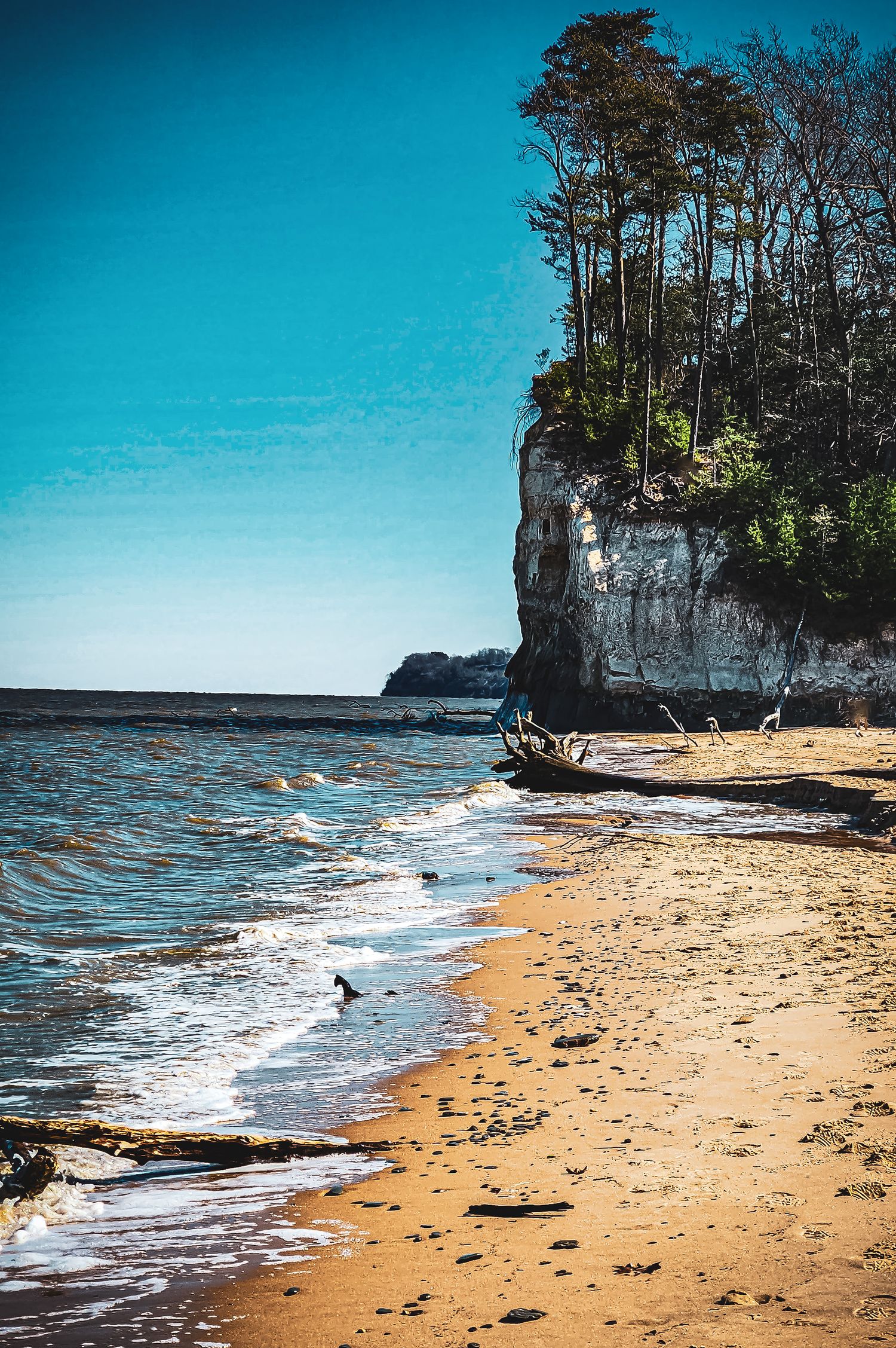 Dramatic limestone cliff meets sandy beach with waves lapping at the shore.