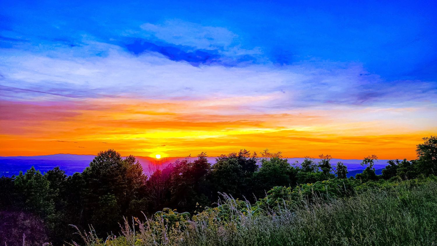 Dramatic sunset sky in orange and purple hues over a mountain ridge.
