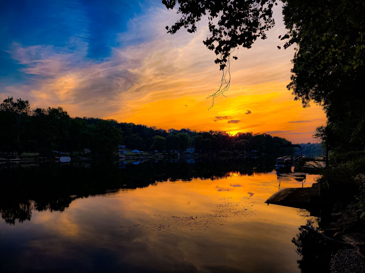 Dramatic sunset over lake with silhouetted trees and orange sky reflecting on water.