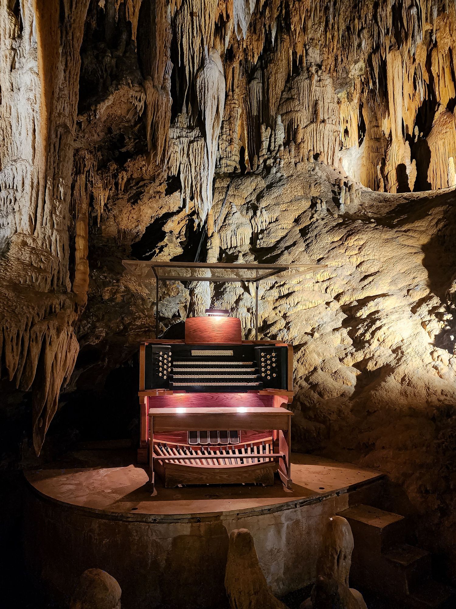 Illuminated vintage organ displayed inside a dramatic limestone cave with stalactites.