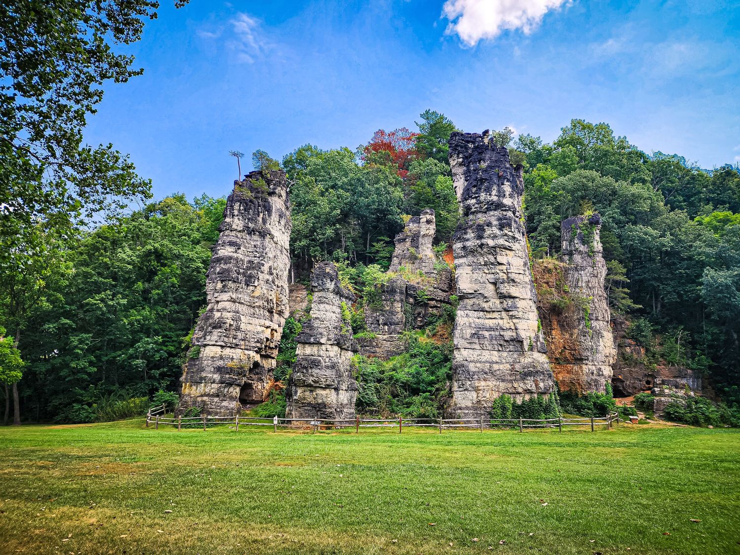 Weathered limestone cliffs and rock formations stand majestically in a green meadow under blue skies.