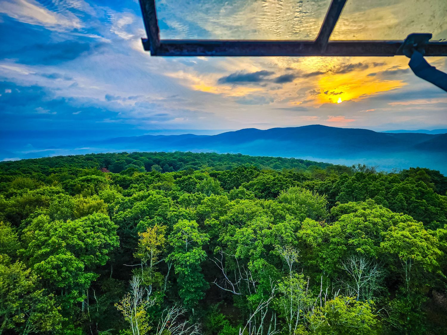 Golden sunset illuminates mountain landscape with observation deck railing visible in foreground.