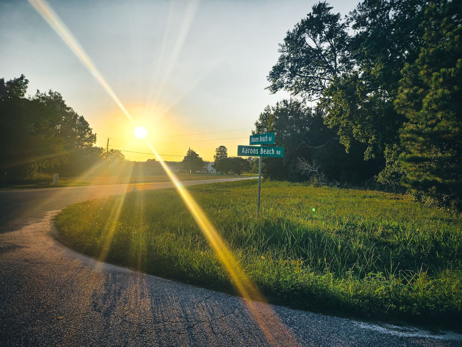 Rural country road at sunset with sun rays breaking through trees.