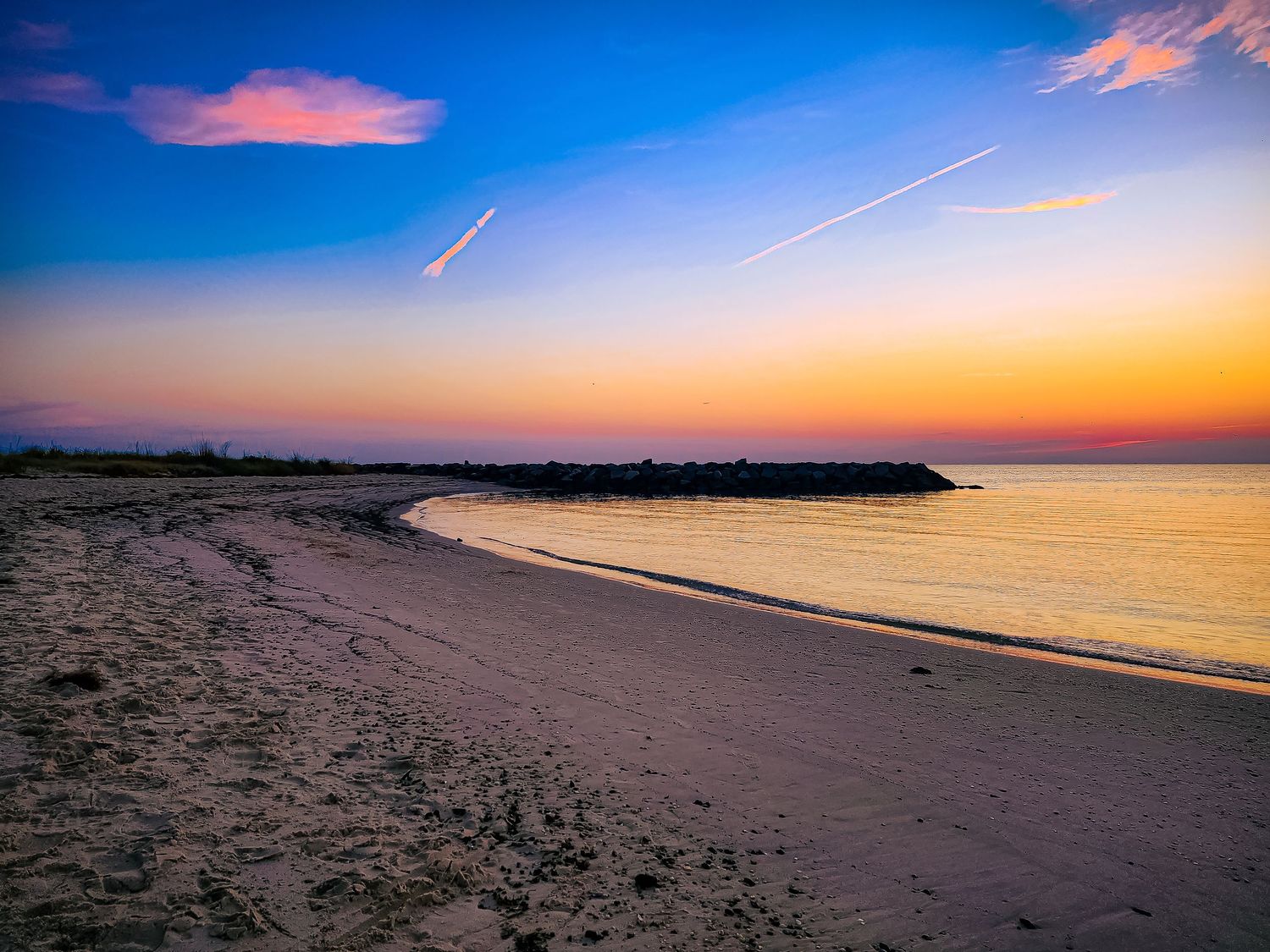 Curved beach shoreline at dusk with orange and blue sky.
