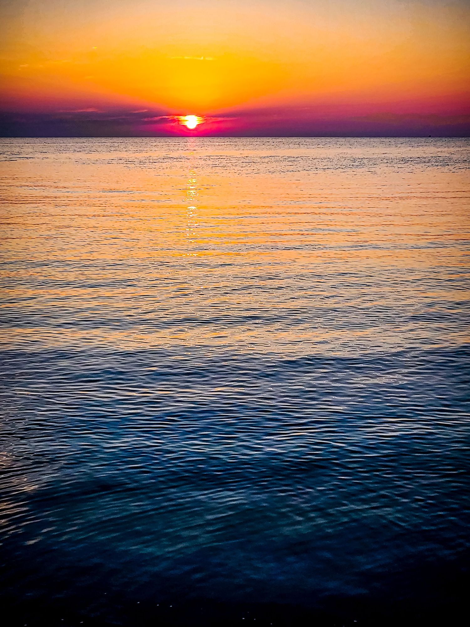 Vibrant orange sunset over calm ocean waters with sun touching horizon.