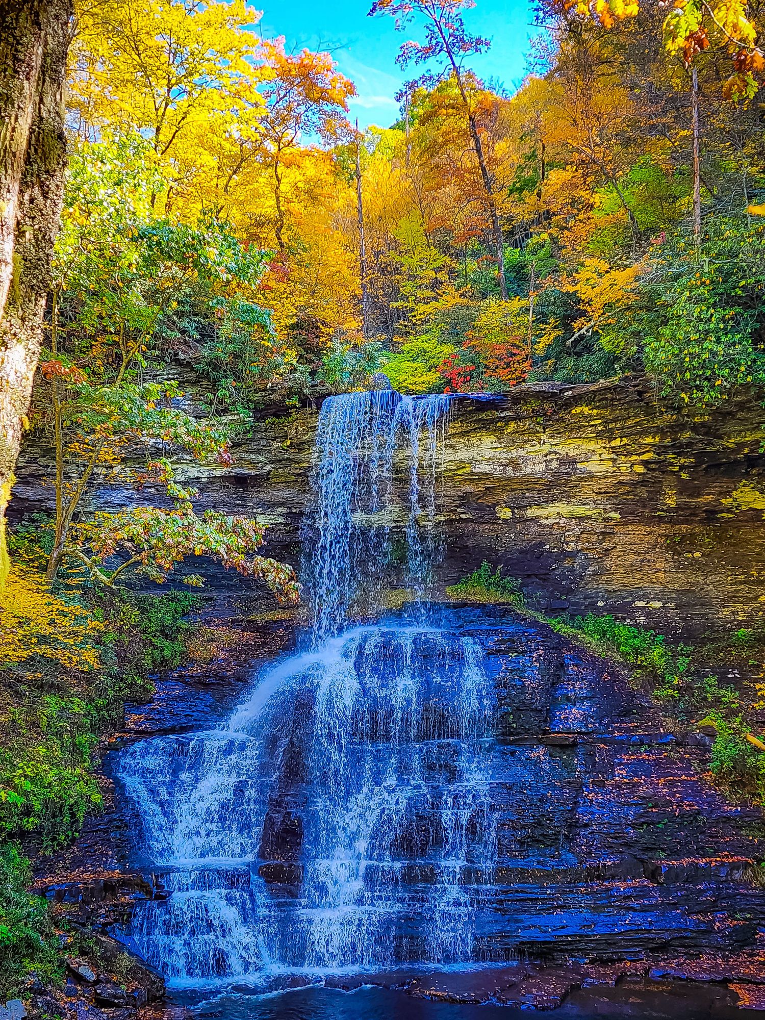 Cascading waterfall surrounded by brilliant autumn foliage in vibrant yellow and orange hues.