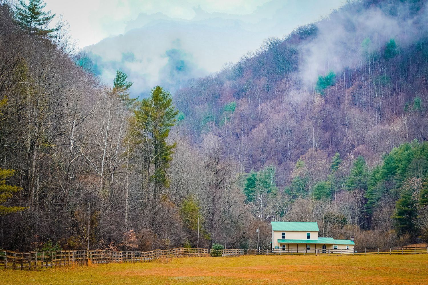 Rustic cabin in misty mountain valley surrounded by bare winter trees.