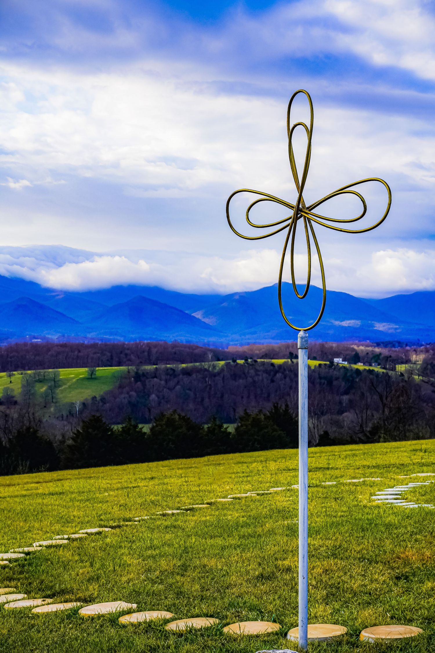 Metal flower sculpture on pole overlooking mountain valley with blue skies.
