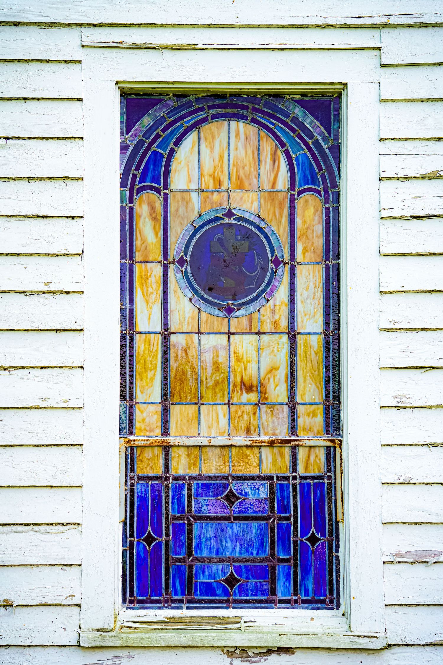 Ornate stained glass church window with blue and amber details in white wooden frame.