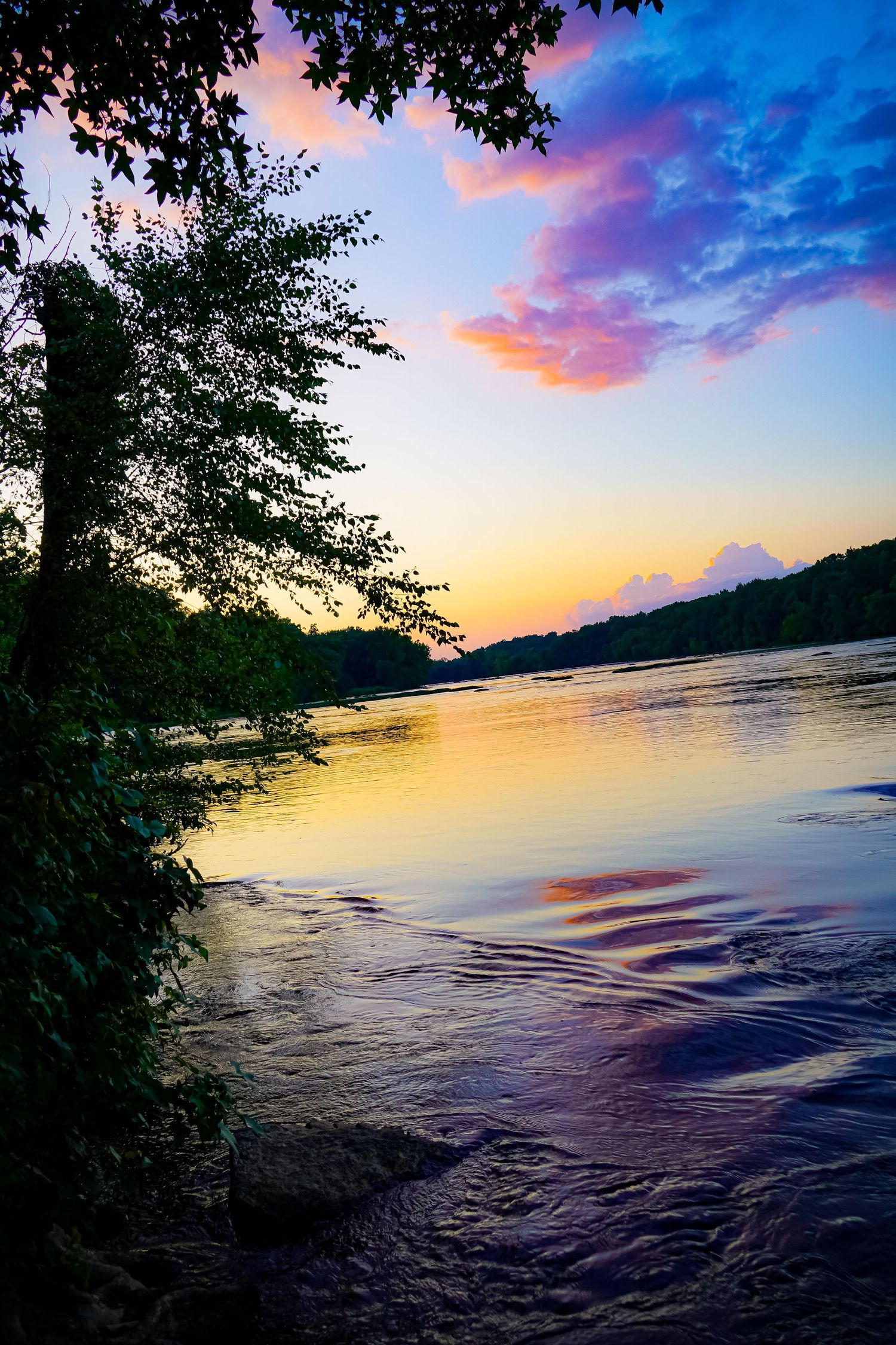 Dramatic sunset over river with vibrant pink and purple clouds reflecting on water.