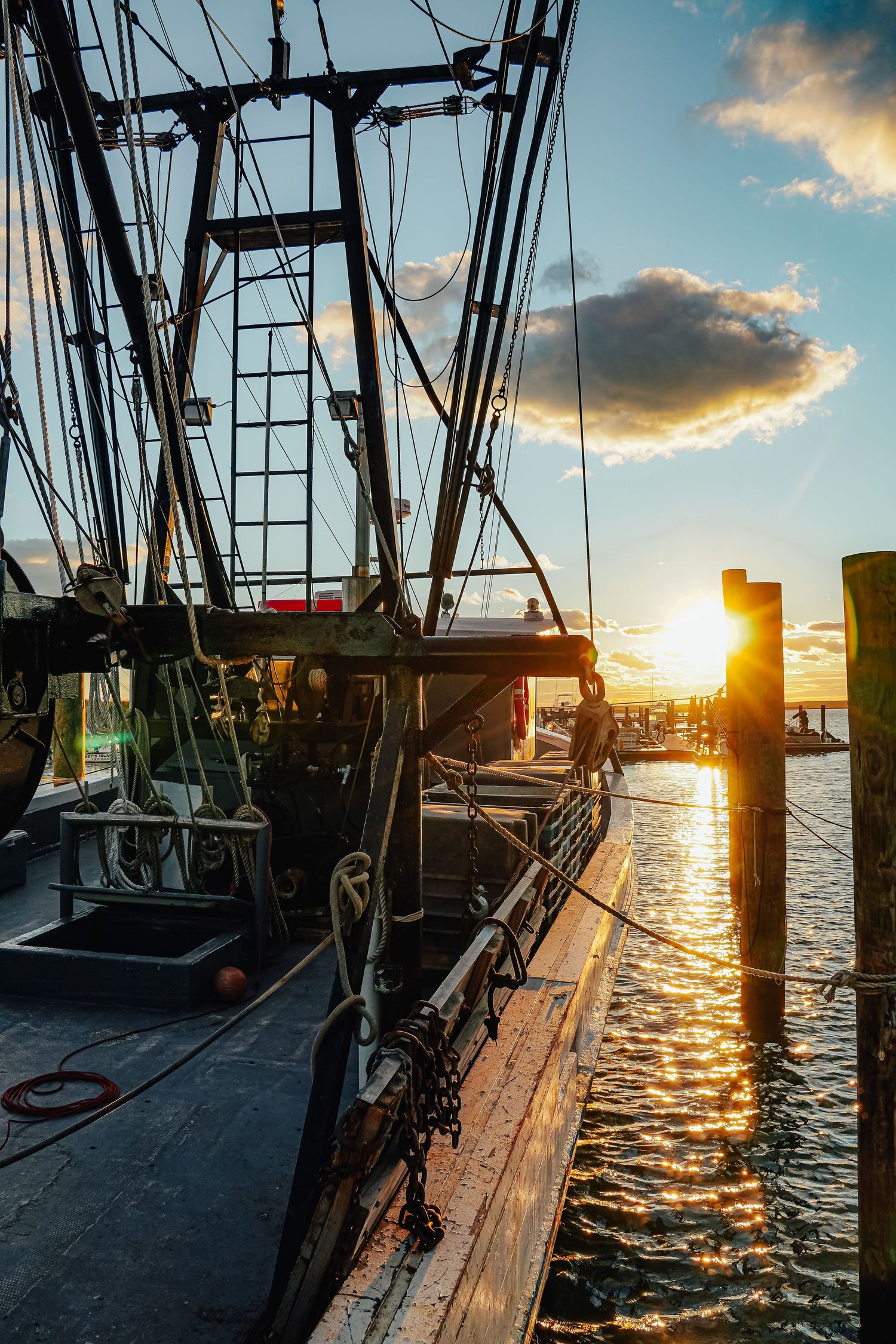 Fishing vessel rigging and equipment silhouetted against golden sunset at dock.