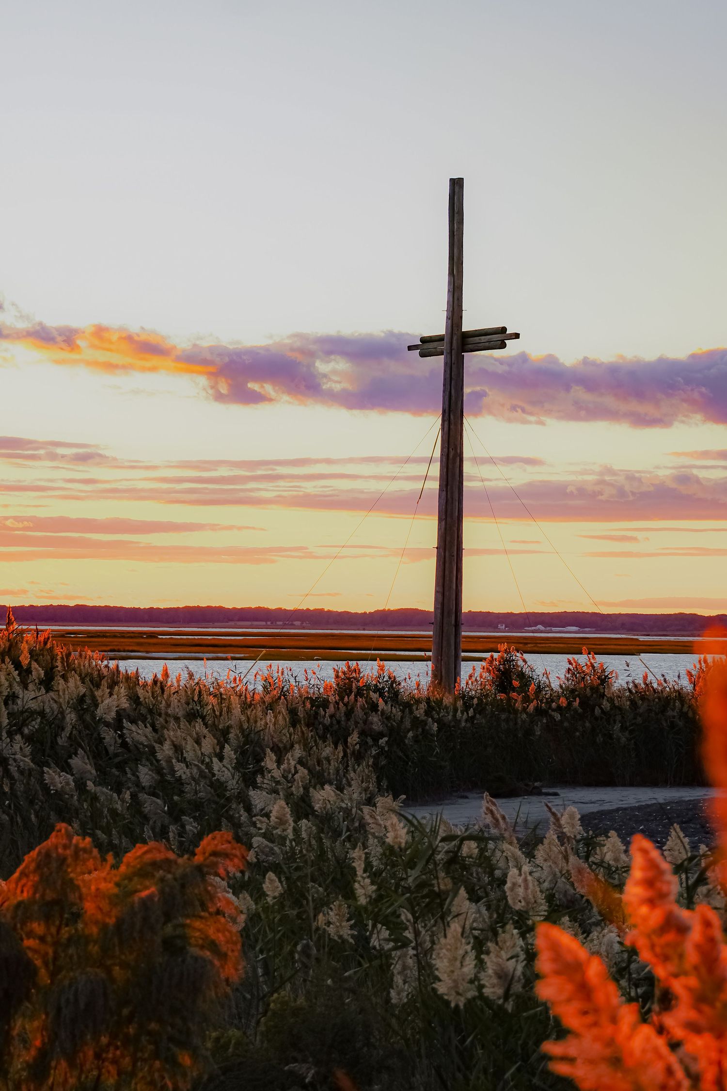 A wooden cross silhouetted against a vibrant sunset sky with orange wildflowers in the foreground.