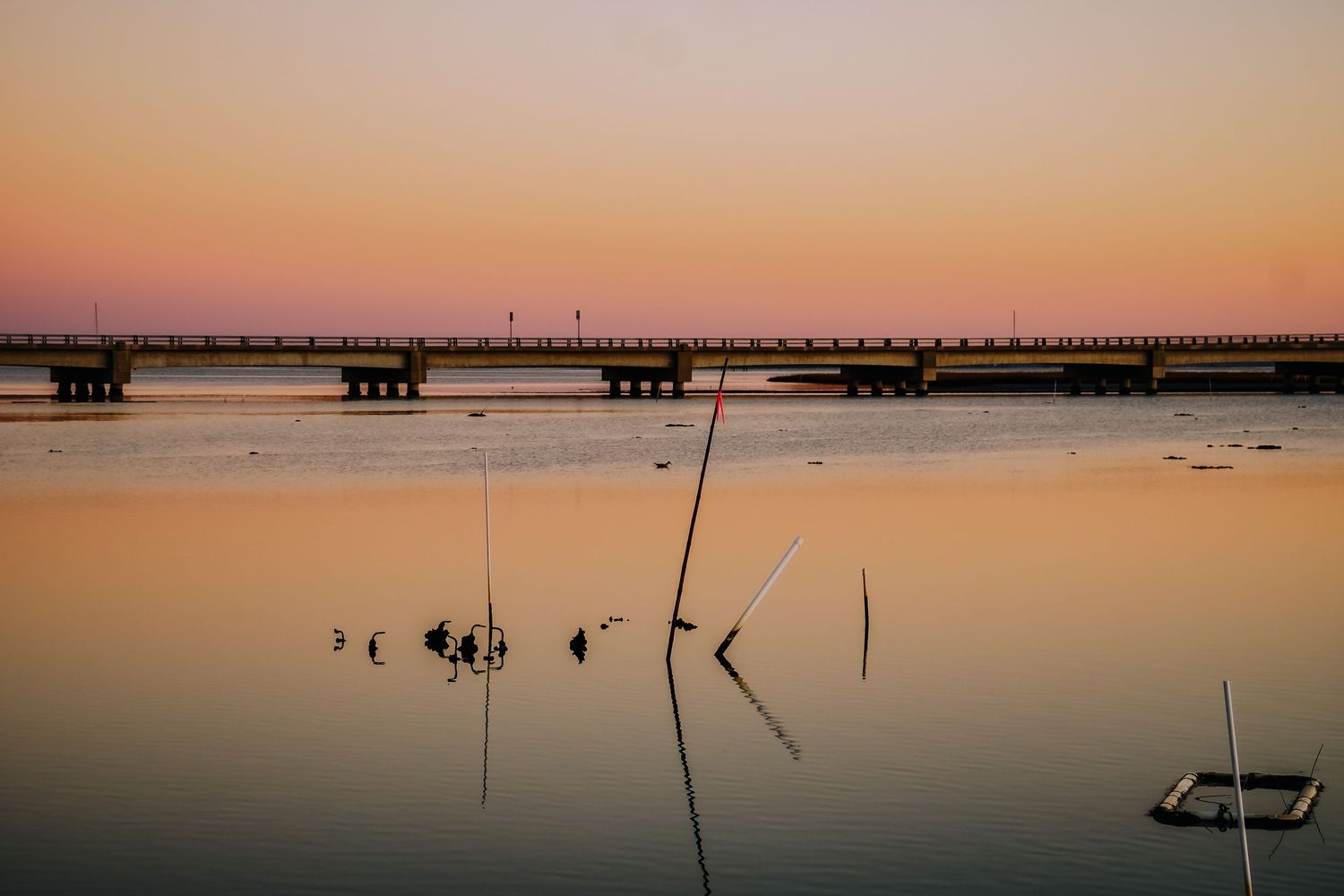 Long wooden pier stretches across calm waters during a peaceful orange sunset.
