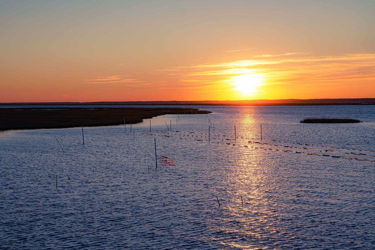 Brilliant orange sunset over coastal waters with wooden posts marking the channel.