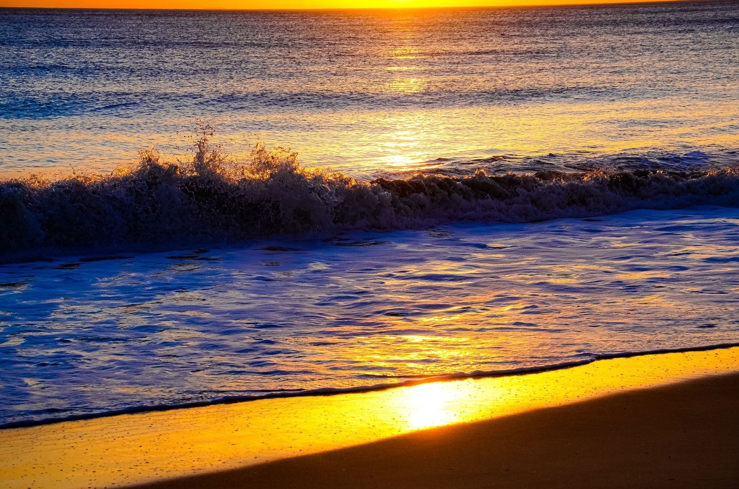 Vibrant orange sunset reflecting off ocean waves breaking on shoreline.