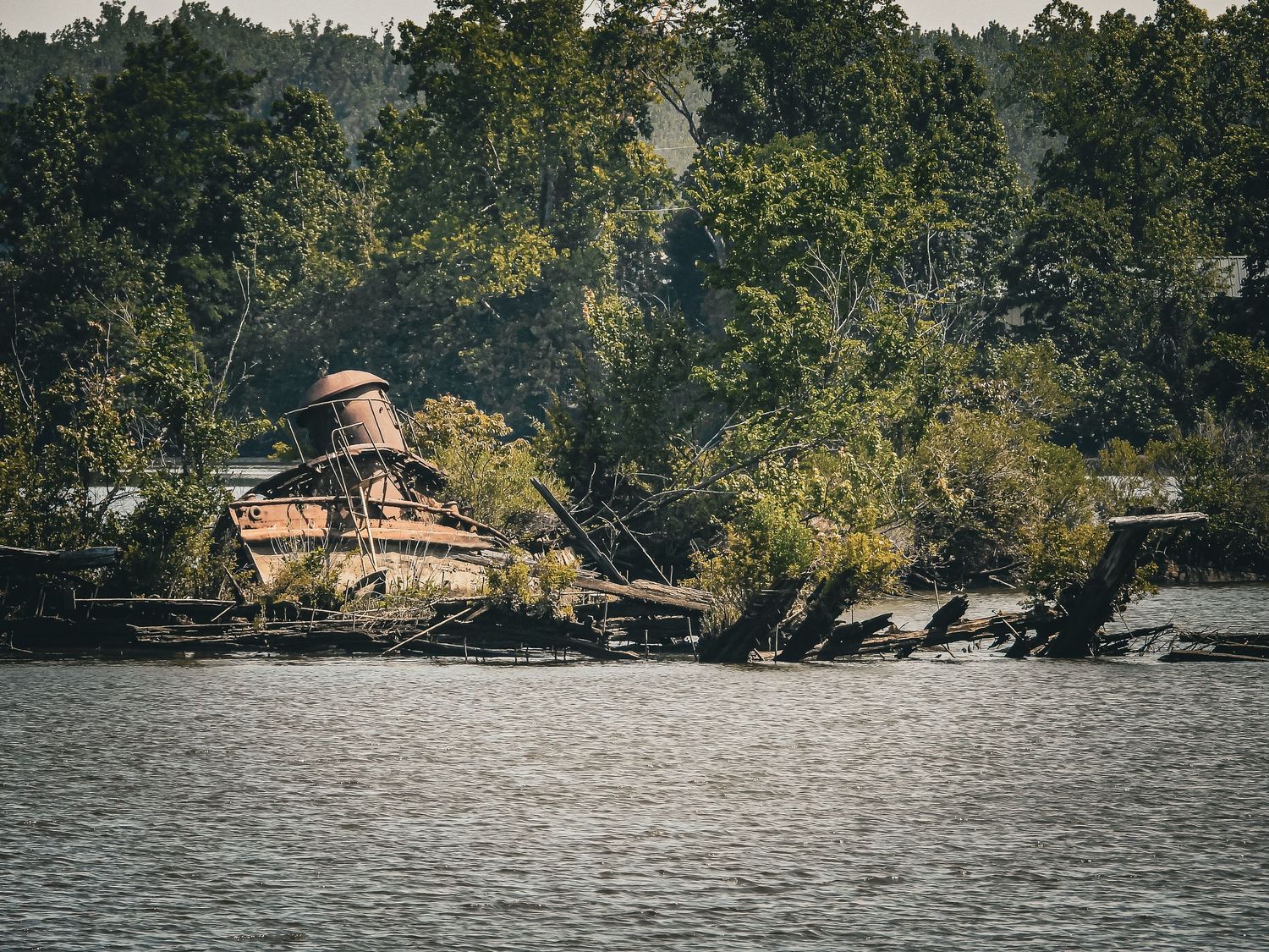 Abandoned wooden structure on rocky shoreline surrounded by dense forest.