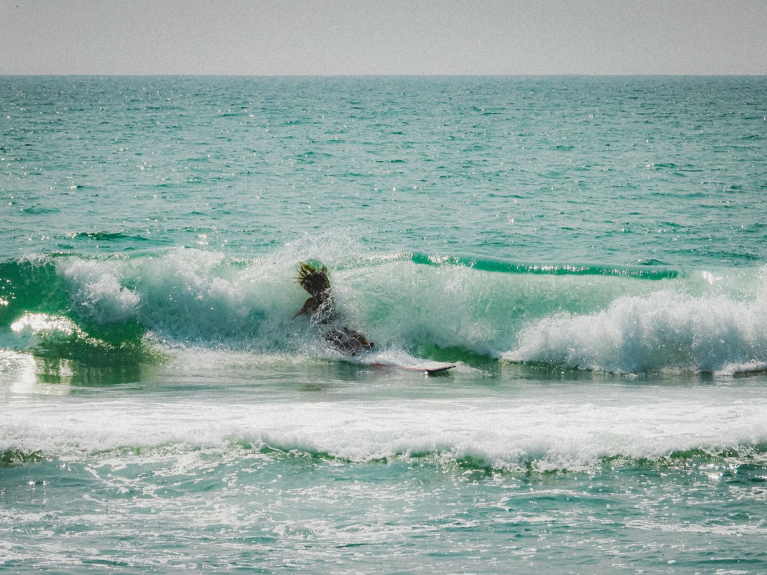 Surfer riding through a crashing turquoise wave in the ocean.