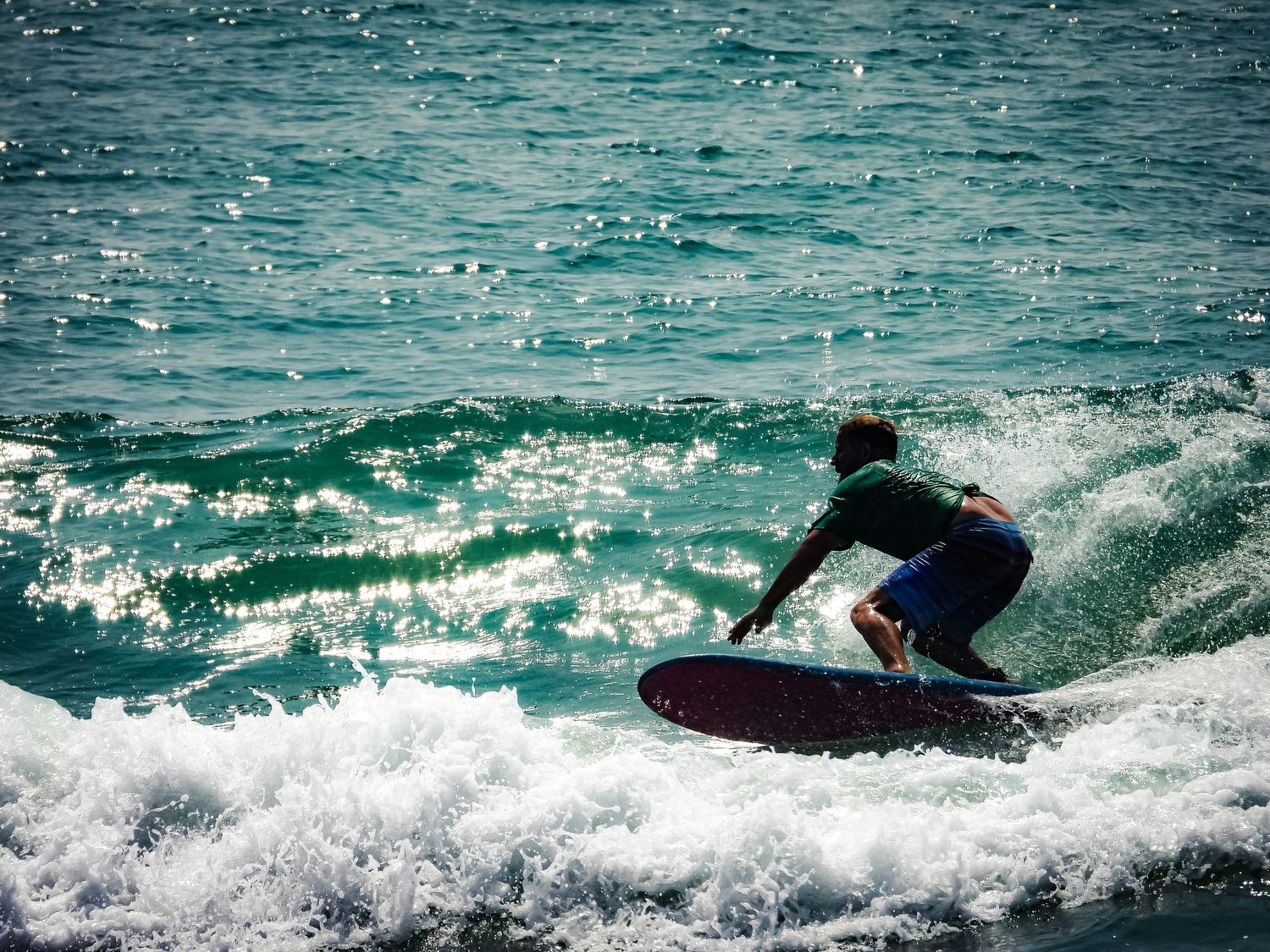 Silhouette of surfer riding a wave with water spray against teal ocean.