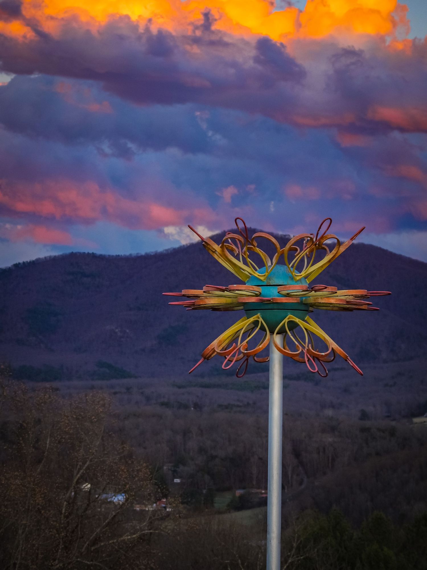 Artistic metal butterfly sculpture silhouetted against dramatic orange and purple sunset sky.