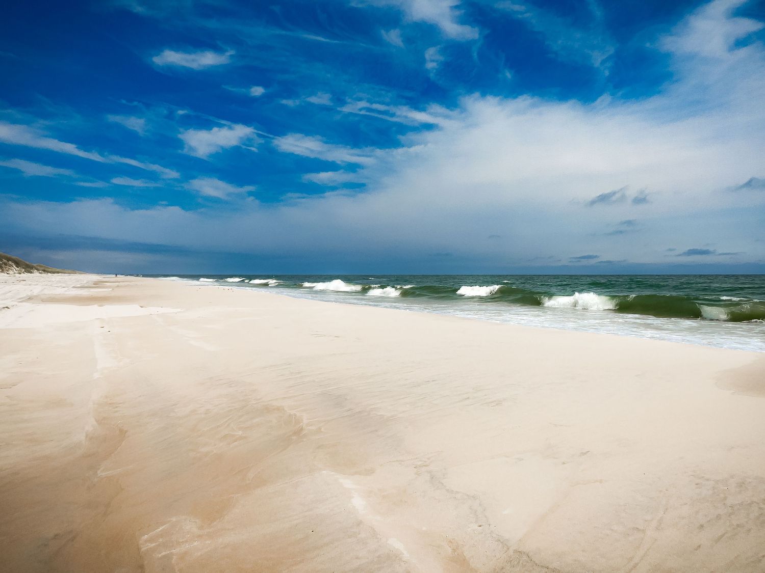 Pristine white sandy beach with rolling waves and blue skies stretching to the horizon.
