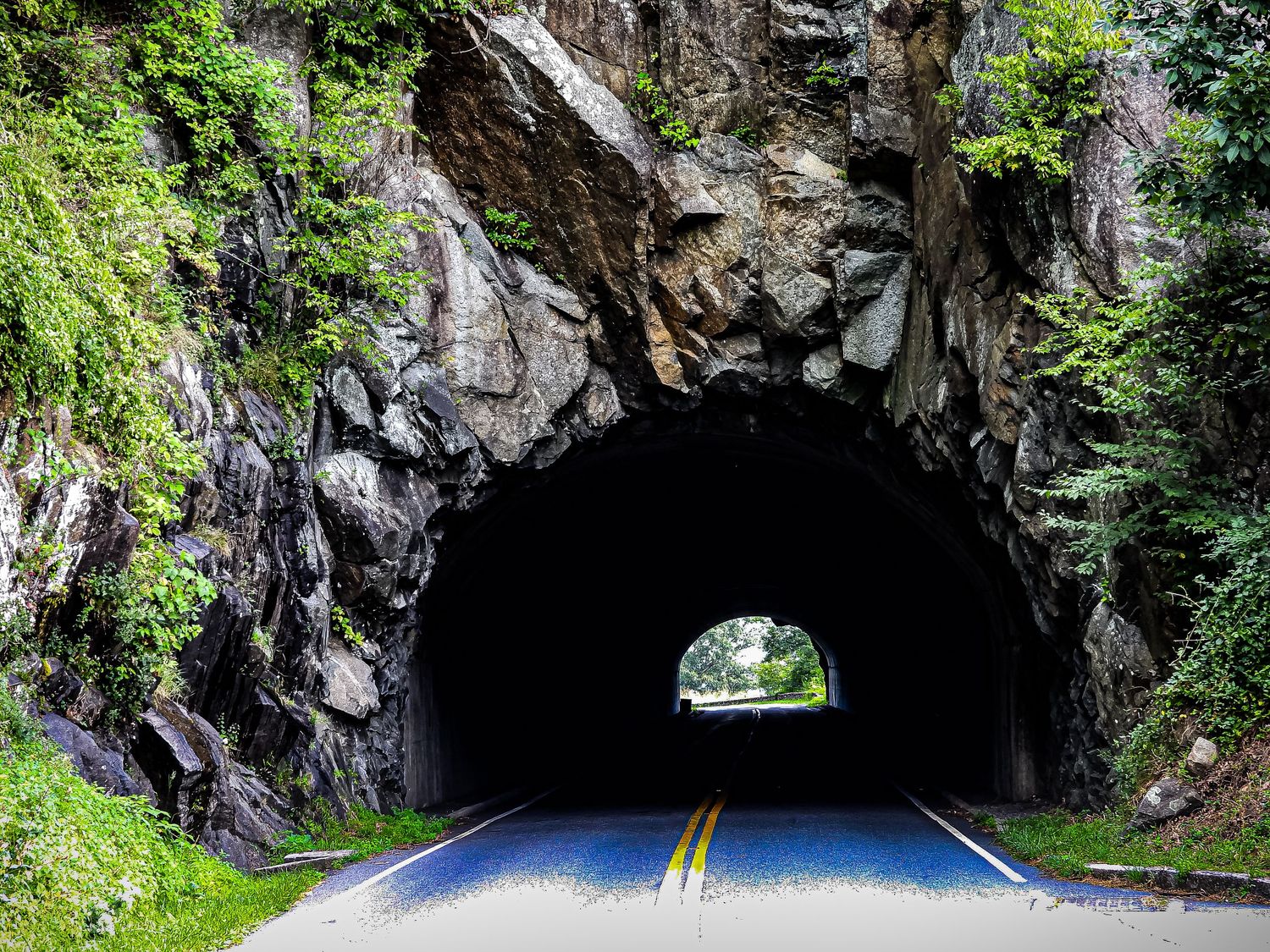 Natural rock tunnel carved through mountain with light visible at the end.