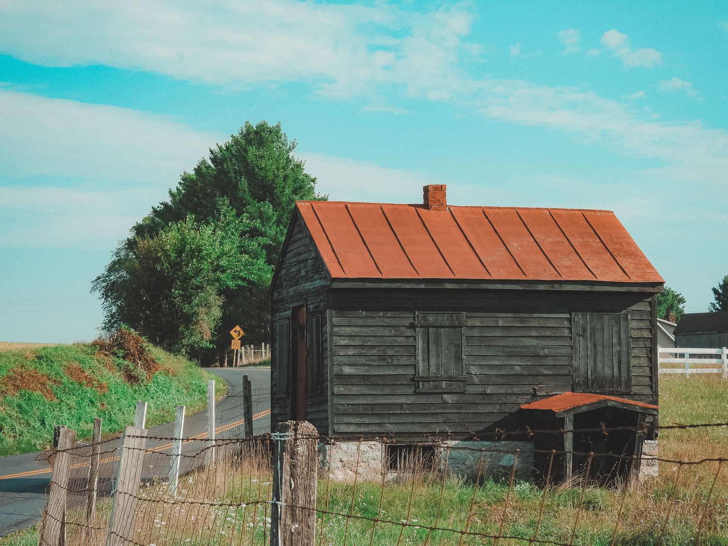Rustic black wooden cabin with orange metal roof sits along rural fenceline.